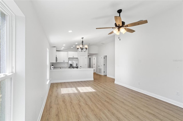 unfurnished living room with lofted ceiling, ceiling fan with notable chandelier, recessed lighting, light wood-style floors, and baseboards