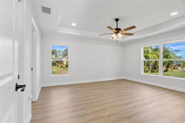 empty room featuring a raised ceiling, light wood-style flooring, visible vents, and ceiling fan