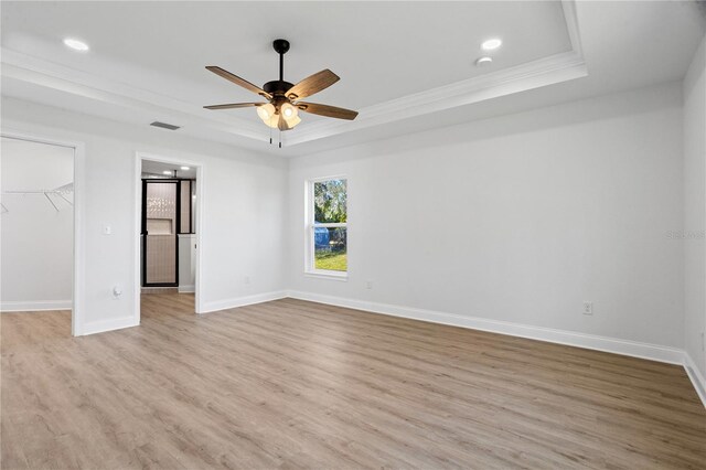 unfurnished bedroom with a spacious closet, baseboards, a raised ceiling, and light wood-style floors