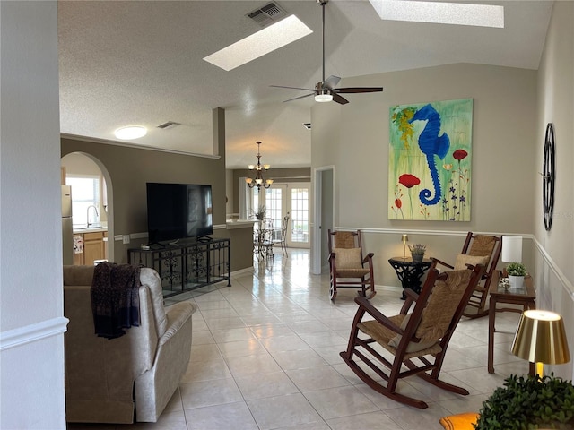 living room with visible vents, ceiling fan with notable chandelier, vaulted ceiling with skylight, arched walkways, and light tile patterned floors