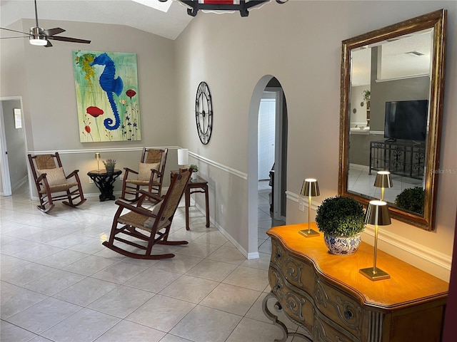 living area with arched walkways, light tile patterned floors, baseboards, ceiling fan, and vaulted ceiling