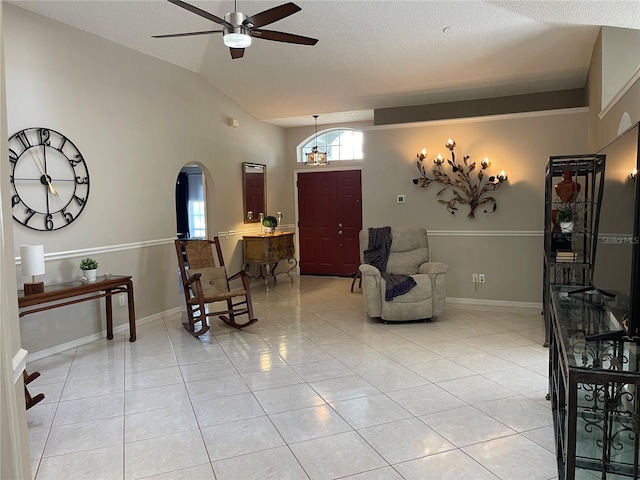 interior space featuring light tile patterned floors, a ceiling fan, baseboards, lofted ceiling, and arched walkways