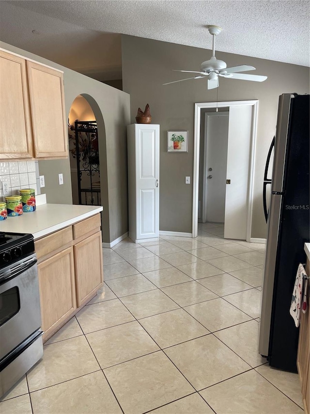 kitchen with arched walkways, light brown cabinets, stainless steel range with gas cooktop, and freestanding refrigerator