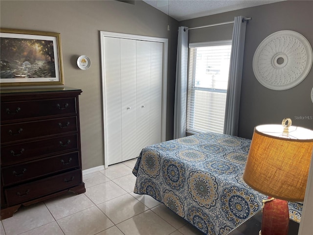 bedroom with lofted ceiling, light tile patterned flooring, a closet, and a textured ceiling