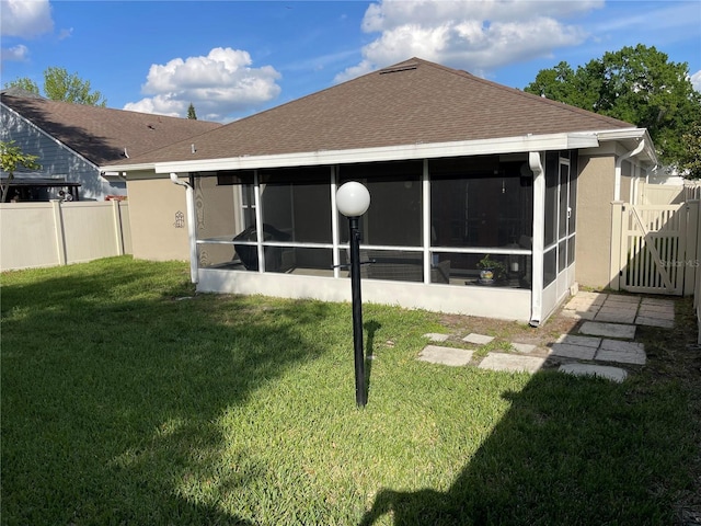 back of property with a gate, fence, a sunroom, stucco siding, and a lawn