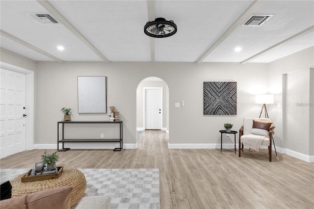 sitting room with arched walkways, visible vents, light wood-style floors, and beam ceiling