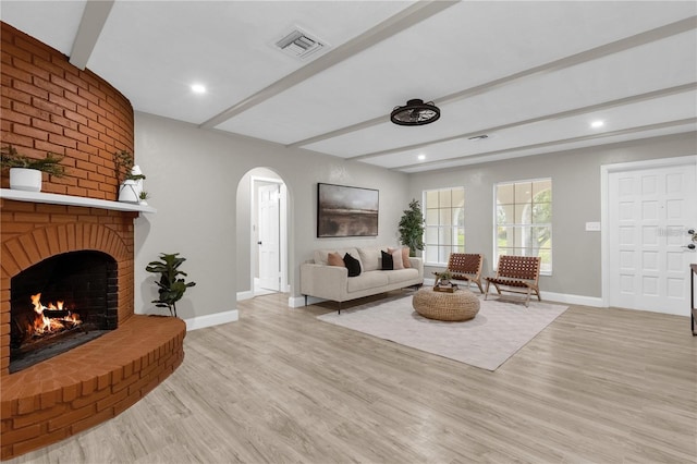 living area featuring visible vents, baseboards, light wood-type flooring, beam ceiling, and arched walkways