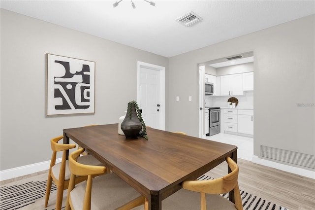 dining room with light wood-type flooring, visible vents, and baseboards