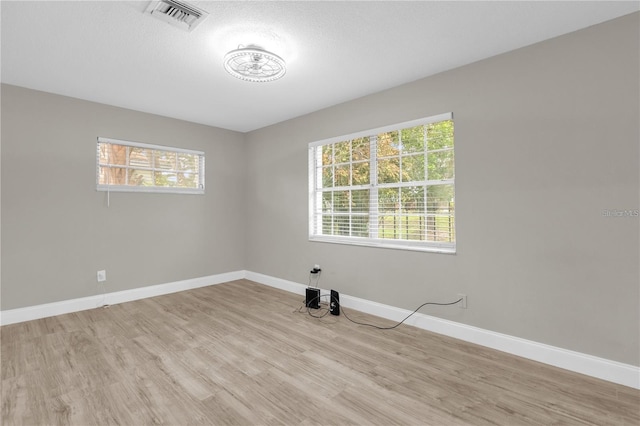 empty room with light wood finished floors, visible vents, a textured ceiling, and baseboards