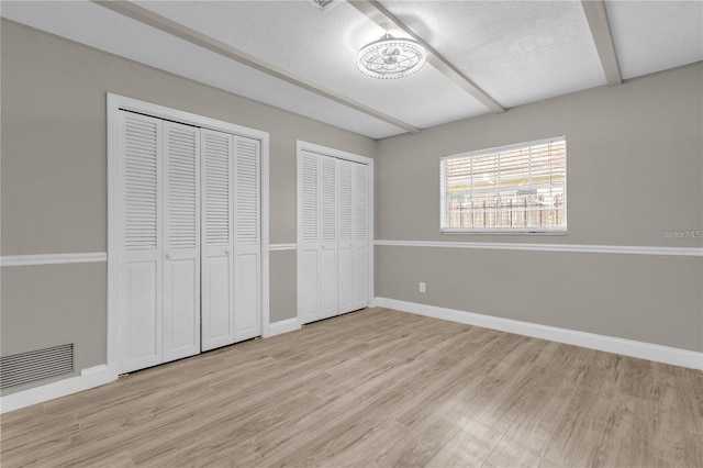 unfurnished bedroom featuring light wood-type flooring, visible vents, multiple closets, and beam ceiling