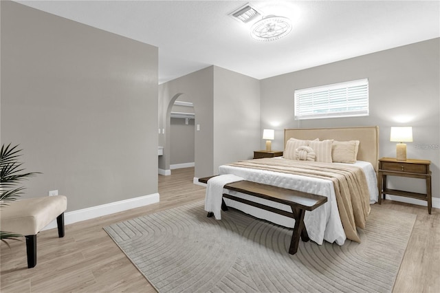 bedroom featuring visible vents, arched walkways, light wood-style floors, and baseboards