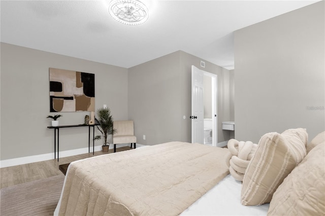 bedroom with connected bathroom, baseboards, and wood finished floors