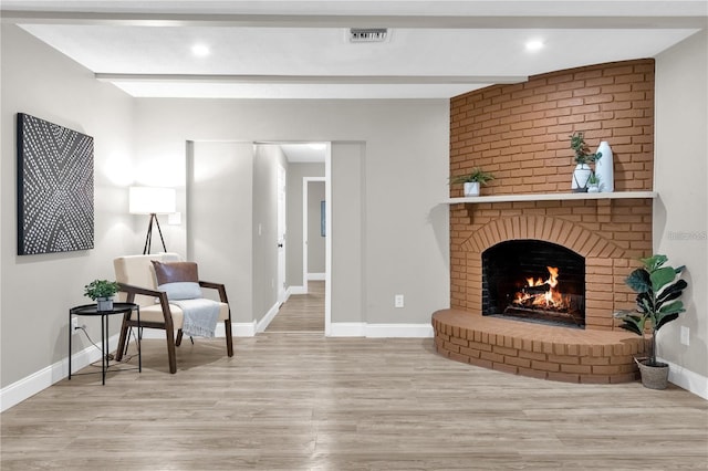 living area featuring wood finished floors, visible vents, baseboards, beam ceiling, and a brick fireplace