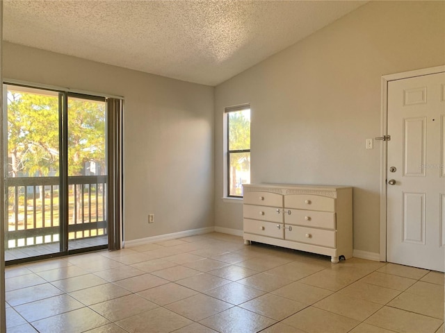 empty room featuring light tile patterned floors, a textured ceiling, baseboards, and vaulted ceiling