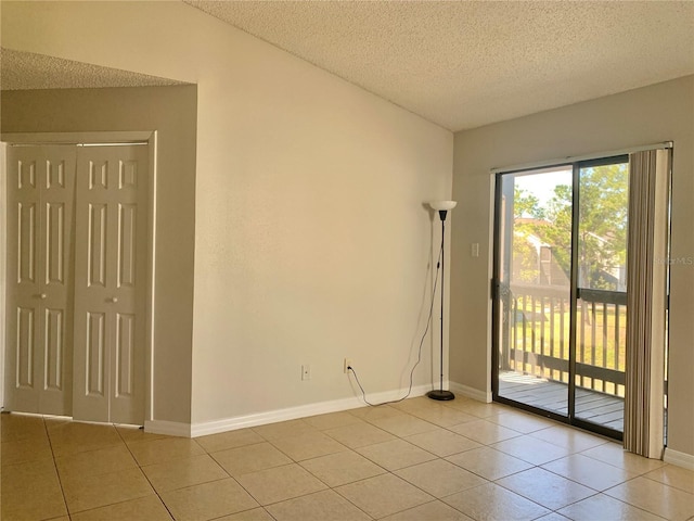 empty room featuring light tile patterned floors, baseboards, a textured ceiling, and vaulted ceiling