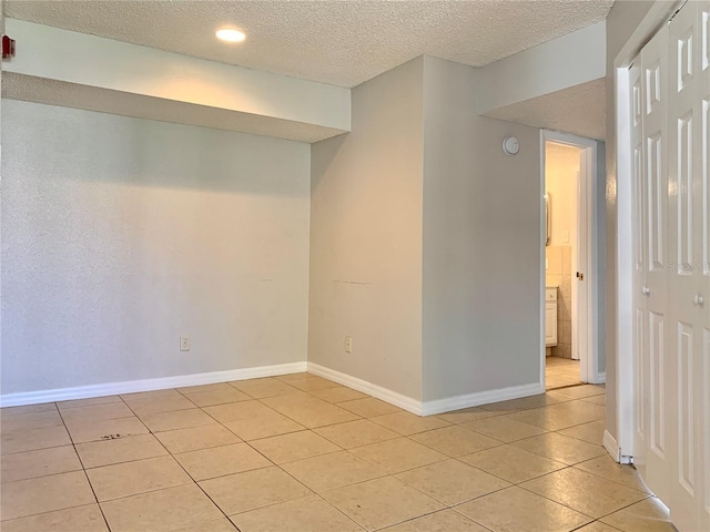 unfurnished room featuring light tile patterned floors, a textured ceiling, and baseboards