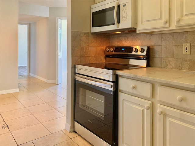 kitchen featuring white microwave, light stone countertops, light tile patterned flooring, stainless steel range with electric stovetop, and tasteful backsplash