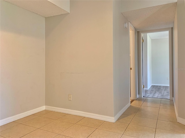 empty room featuring light tile patterned floors, baseboards, and a textured ceiling