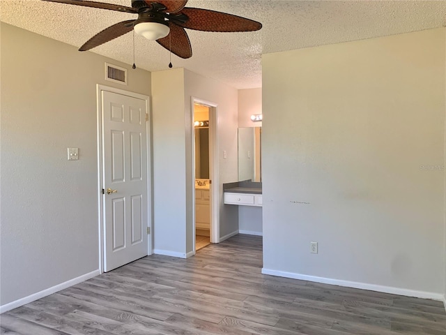 unfurnished bedroom featuring baseboards, wood finished floors, visible vents, and a textured ceiling