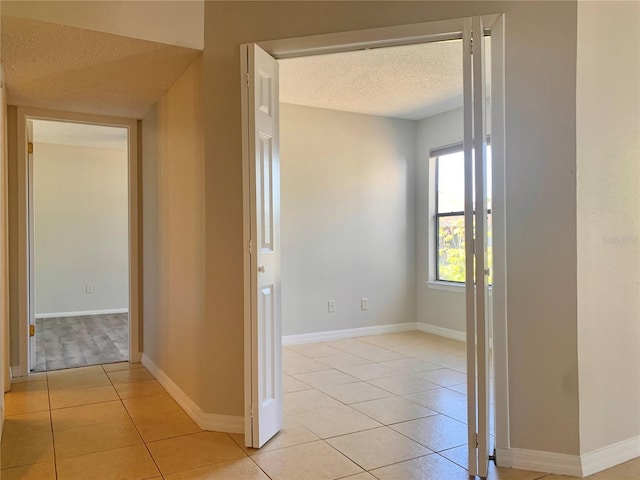 hall with light tile patterned floors, baseboards, and a textured ceiling