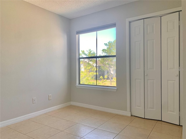 unfurnished bedroom featuring a closet, baseboards, a textured ceiling, and light tile patterned flooring