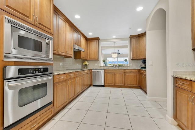 kitchen with under cabinet range hood, backsplash, appliances with stainless steel finishes, and brown cabinets