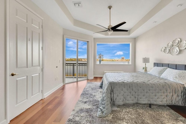 bedroom featuring a raised ceiling, access to outside, wood finished floors, and visible vents