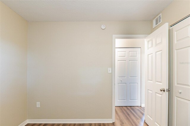 spare room with light wood-type flooring, baseboards, visible vents, and a textured ceiling