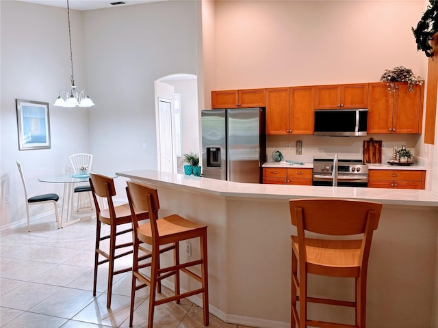 kitchen featuring arched walkways, brown cabinets, stainless steel appliances, and light countertops