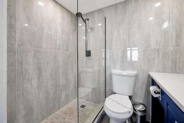 bathroom with vanity, tile walls, toilet, and a tile shower