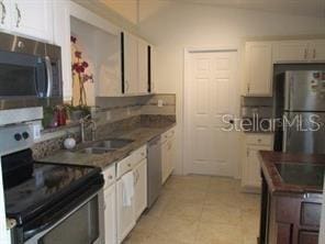 kitchen with lofted ceiling, a sink, stainless steel appliances, white cabinets, and dark countertops