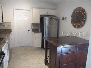 kitchen featuring white cabinetry, stovetop, light tile patterned flooring, and freestanding refrigerator