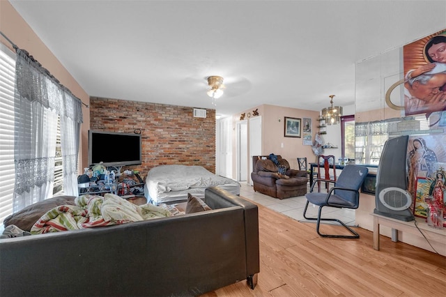 living room with visible vents, ceiling fan with notable chandelier, brick wall, and light wood finished floors