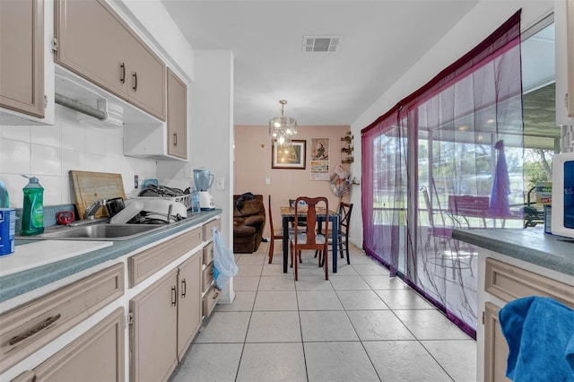 kitchen featuring visible vents, light tile patterned flooring, a sink, decorative backsplash, and a chandelier