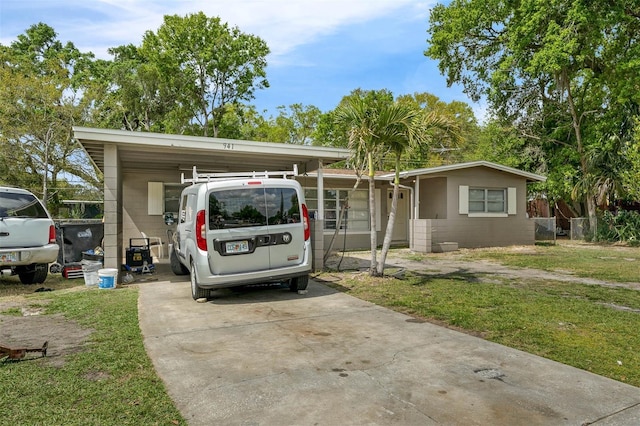 view of front of home with a carport, concrete block siding, concrete driveway, and a front yard