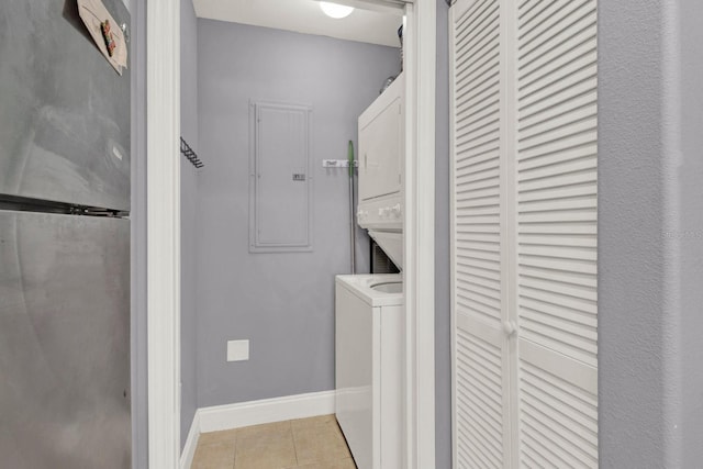 laundry room featuring baseboards, light tile patterned floors, laundry area, electric panel, and stacked washer / drying machine