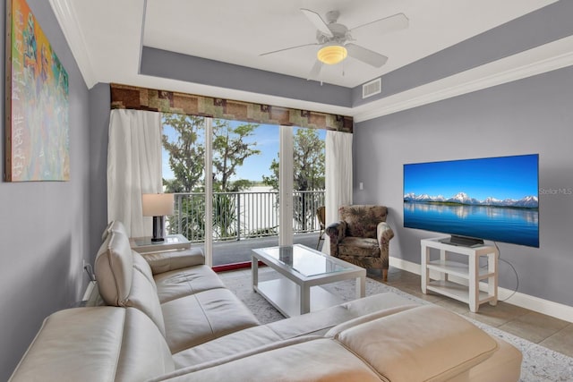 tiled living room with a ceiling fan, a tray ceiling, baseboards, and visible vents