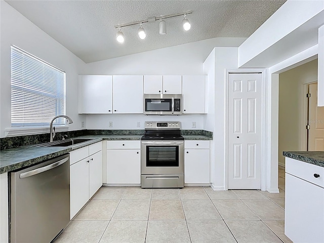 kitchen with dark countertops, vaulted ceiling, appliances with stainless steel finishes, light tile patterned flooring, and a sink