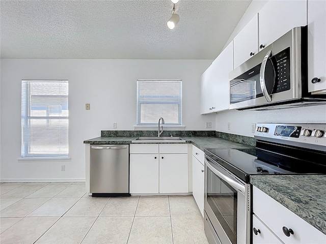 kitchen with dark countertops, light tile patterned floors, appliances with stainless steel finishes, a textured ceiling, and a sink