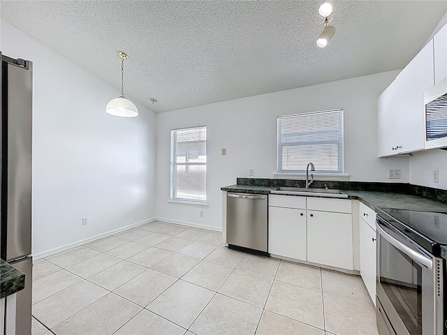 kitchen with a sink, dark countertops, appliances with stainless steel finishes, white cabinets, and light tile patterned flooring