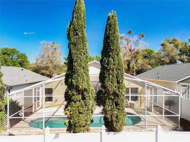 rear view of property featuring glass enclosure, an outdoor pool, a patio, and stucco siding