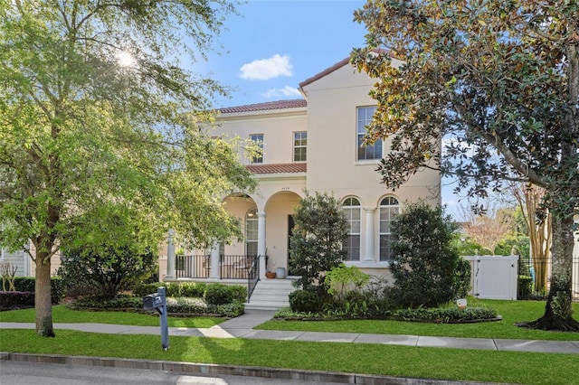 mediterranean / spanish home with fence, a tiled roof, a front yard, covered porch, and stucco siding