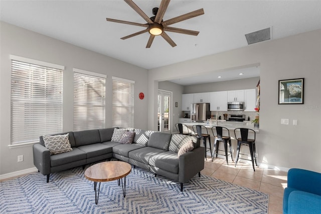 living area with light tile patterned floors, a ceiling fan, visible vents, and baseboards