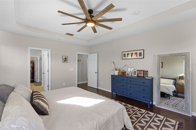 bedroom with a raised ceiling, wood finished floors, baseboards, and visible vents