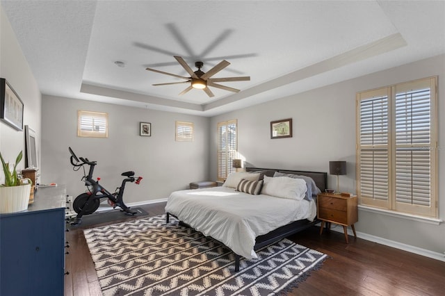 bedroom featuring baseboards, a raised ceiling, and dark wood-style flooring