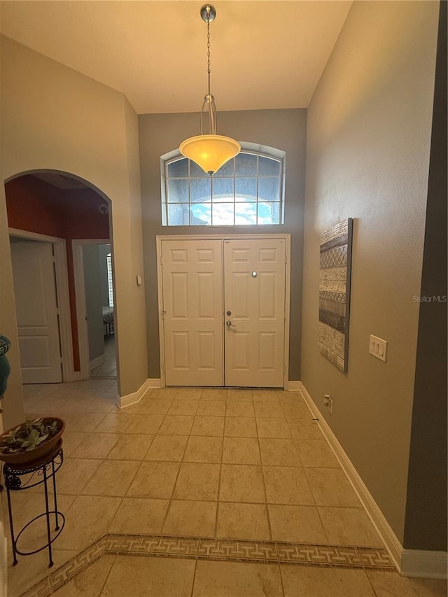 foyer featuring a high ceiling, light tile patterned flooring, baseboards, and arched walkways