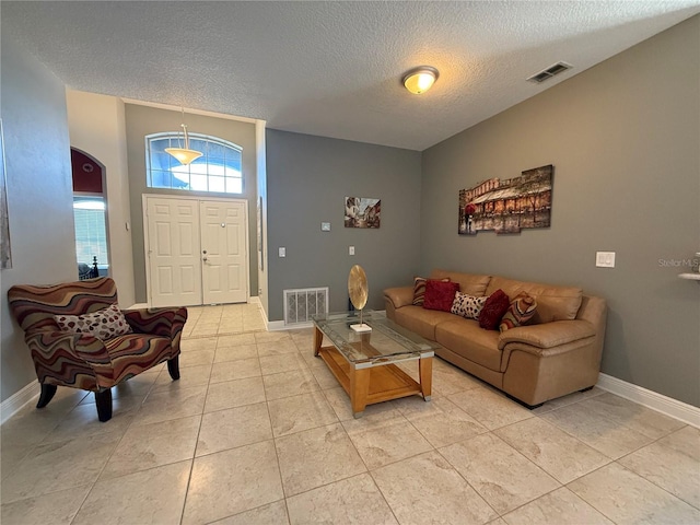 living room with light tile patterned floors, visible vents, baseboards, and a textured ceiling