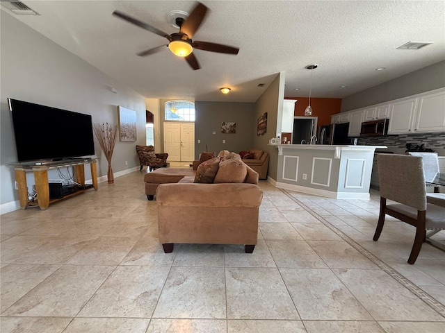 living room with visible vents, baseboards, a textured ceiling, and a ceiling fan