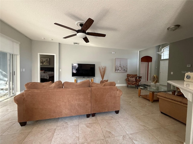 living area with baseboards, visible vents, arched walkways, ceiling fan, and a textured ceiling