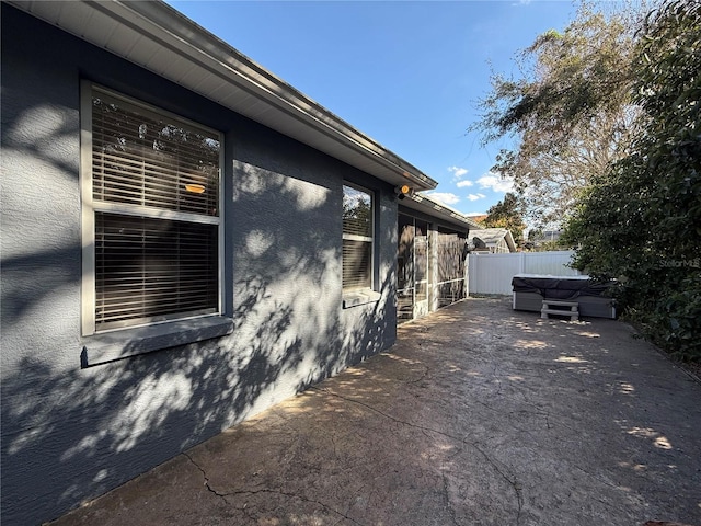 view of side of property with a patio area, stucco siding, a hot tub, and fence